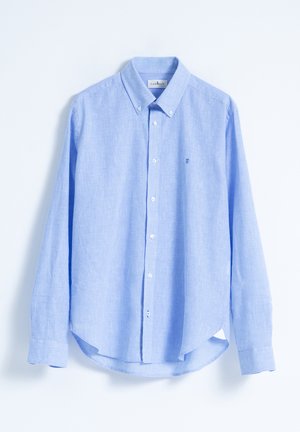 Camisa de botones azul clara con un cuello clásico, mangas largas y un dobladillo redondeado. Cuenta con un pequeño logo bordado en el pecho.