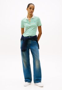 Ριγέ πράσινο και άσπρο polo shirt με γιακά, συνδυασμένο με χαλαρά μπλε τζιν παντελόνια. Ναυτικό πουλόβερ δεμένο στη μέση. Λευκά αθλητικά παπούτσια.