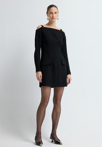 Mustapaita olkaimeton mekko pitkillä hihoilla, sivuleikkauksilla, kahdella etutaskulla ja vartalonmyötäisellä muotoilulla. Yhdistettynä läpinäkyviin sukkahousuihin ja kärjellisiin kenkiin.