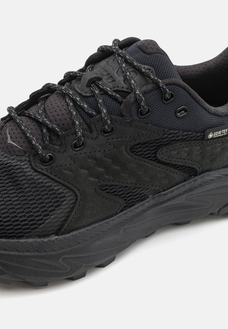 Czarny but sportowy z mieszanką materiałów siateczkowych i zamszowych, z teksturowanymi wzorami, płaskimi sznurówkami i wytrzymałą gumową podeszwą.