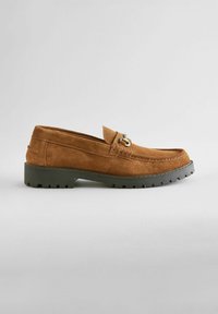 Ruskeat mokka loafer-kengät, joissa on ommeltu varvas, koristeellinen metallinen yksityiskohta ja teksturoitu musta kumipohja pidon vuoksi. Tasainen siluetti.