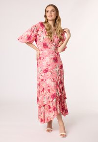 Robe maxi florale en rose, avec des manches bouffantes, un col en V, des volants superposés et un mélange de motifs de fleurs rouges et blanches.