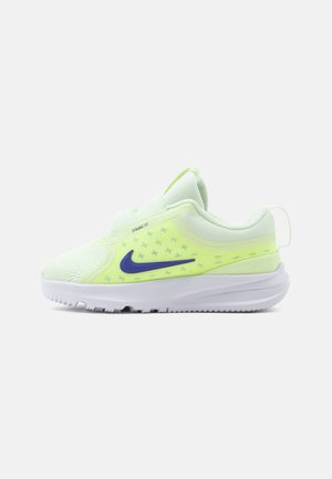 Lichtgroene en witte sportschoen met paarse Nike-vink, bovenwerk van gaas, gevoerde zool en trekriempje bij de hiel, zijaanzicht.