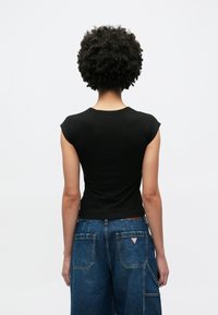 Zwart kortarmig T-shirt met een aansluitend ontwerp, gladde textuur en een ronde hals, gecombineerd met hooggetailleerde blauwe spijkerbroeken.