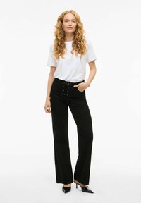 Bijela majica s kratkim rukavima u kombinaciji s crnim hlačama visokog struka koje imaju čipkastu vezicu sprijeda i džepove. Crne cipele na visokom pete.