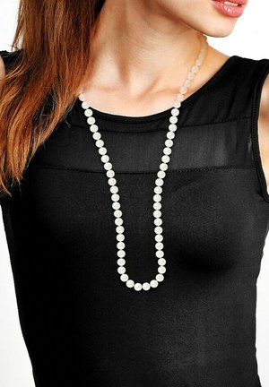Collier long à deux brins avec des perles sphériques blanches. Porté sur un haut noir, présentant un design simple et texturé.