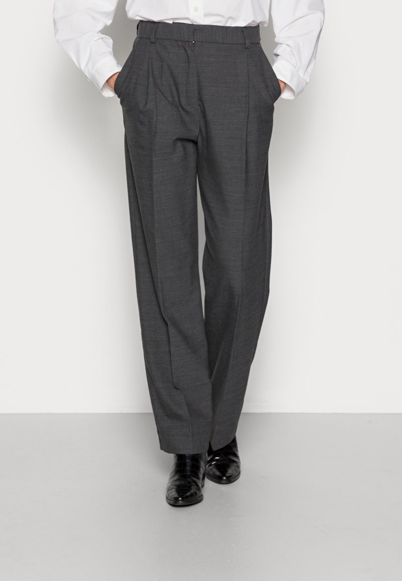 Grijze geplooide broek met een getailleerde pasvorm, voorzien van zijzakken, een gladde textuur en een klassieke tailleband, gecombineerd met glanzende zwarte schoenen.