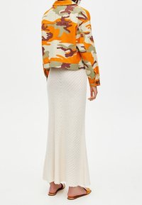 Bunda s trendy maskáčovým vzorem v oranžové, zelené a hnědé barvě, s knoflíkovými detaily; kombinovaná s texturovanou krémovou pletenou sukní až na zem.