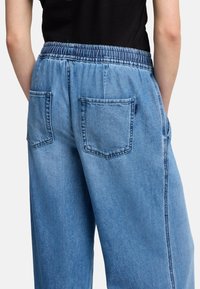 Ljust blå denimbyxor med elastiskt midjeband. Har två bakfickor och en avslappnad, vid design. Slät textur och en ledig passform.