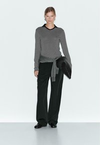 Striped black and white long-sleeve top with a collar, paired with black wide-leg trousers and a textured black clutch. Simple design.