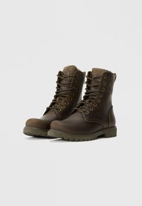 Botas de couro castanho com atacadores, apresentando uma superfície texturizada, costura amarela contrastante, colarinho acolchoado e sola de borracha robusta. Detalhe com fecho lateral presente.