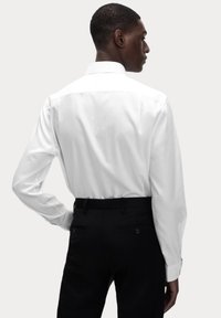Camisa blanca de manga larga con cuello clásico, textura suave y puños abotonados, combinada con pantalones negros ajustados.