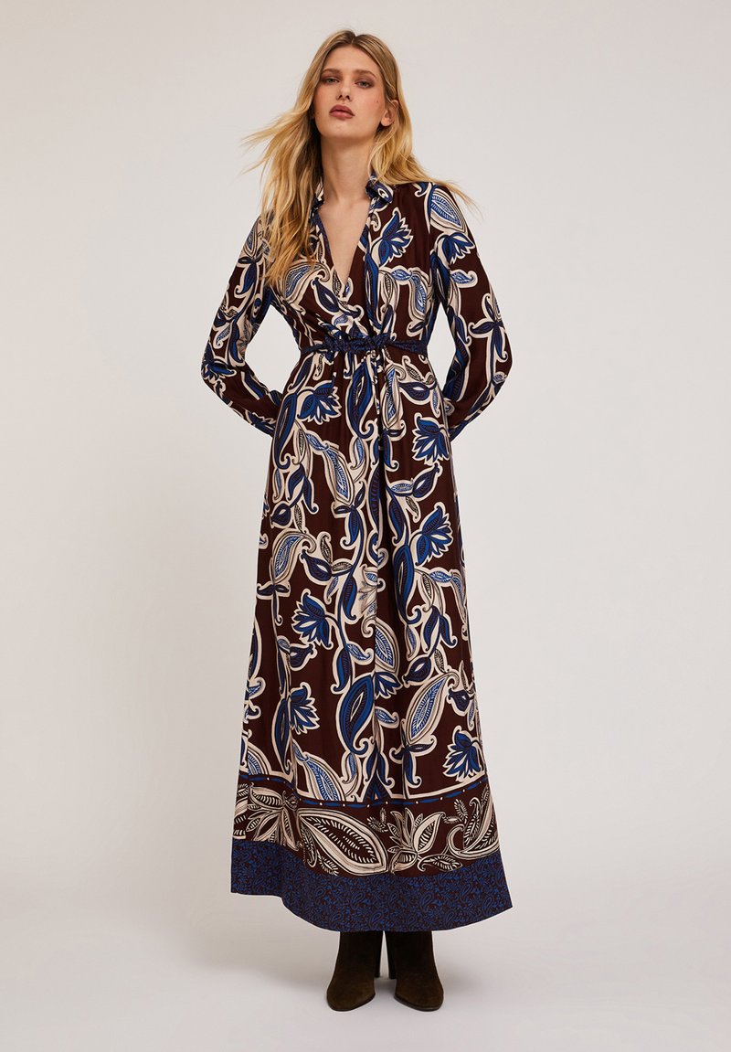 Rochie lungă maro cu motive florale albastre și crema, design tip wrap, mâneci lungi și talie definită. Material neted și tiv până la glezne.