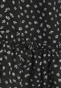 Robe en tissu noir ornée d'un motif floral blanc, avec des fronces à la taille et une surface texturée.