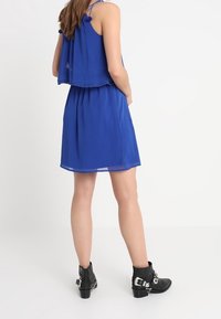 Robe bleu deux pièces avec un haut à volants et des bretelles, associée à des bottines noires à boucles. Tissu lisse, design décontracté.