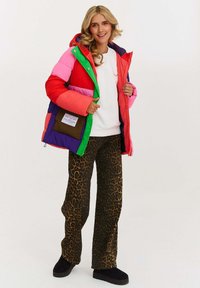 Farebná prešívaná bunda s ružovými, červenými, zelenými, modrými a fialovými časťami. Nosená cez biele tričko, v kombinácii so zvieracím vzorom nohavicami a čiernymi topánkami.