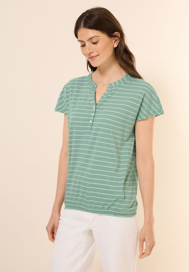 Chemise verte clair à manches courtes avec des rayures horizontales blanches, présentant un col henley et trois boutons, avec un ourlet légèrement froncé.