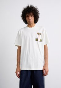 Off-white bomuld t-shirt med et farverigt grafisk motiv af et tårn med blomsteraccenter på venstre bryst. Løs pasform, korte ærmer.