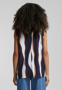 Haut sans manches bleu marine avec des rayures ondulées blanches et orange, fabriqué en tissu lisse. Présente un col rond et un ourlet fendu.
