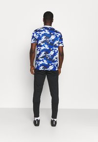 Kortärmad blå kamouflage t-shirt med svarta accenter, kombinerad med svarta träningsbyxor och svarta skor, som visar en modern atletisk stil.