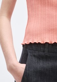 Ριμπ δαντελωτό ροζ τοπ με κυματιστό τελείωμα, σε συνδυασμό με σκούρο τζιν παντελόνι. Το τοπ είναι εφαρμοστό με υφή.