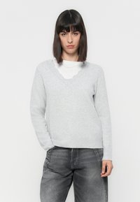 Lichtgrijze trui met een gekartelde V-hals, geribde manchetten en een iets losvallende pasvorm, gecombineerd met donkergrijze relaxte jeans.