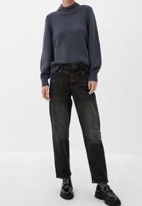 Gestrickter dunkelgrauer Pullover mit hohem Kragen, kombiniert mit schwarzen geraden Jeans und glänzenden schwarzen Slippern.