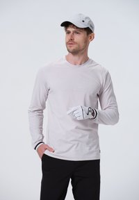 Lys pink langærmet skjorte med et subtilt geometrisk mønster, båret med sorte bukser og en grå kasket. Hvid golfhandske med accenter.