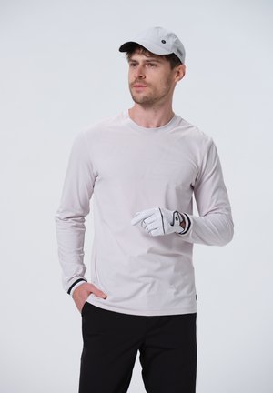 Lys pink langærmet skjorte med et subtilt geometrisk mønster, båret med sorte bukser og en grå kasket. Hvid golfhandske med accenter.