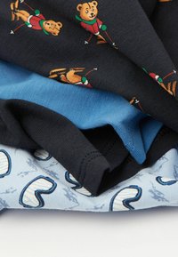 Složené dětské oblečení v námořnické barvě s potiskem medvěda na lyžích, jednobarevný modrý materiál a světle modrý materiál s bílými a modrými vzory srdcí.