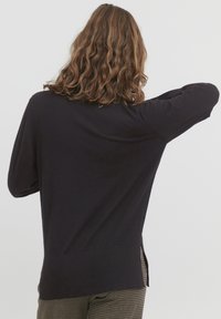 Pulover lung cu manșon lung, de culoare bleumarin închis, având o croială lejeră, manșete cu nervuri și un tiv rotunjit. Materialul pare moale și neted, având slituri laterale pentru confort.