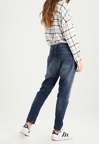 Jeans dżinsowe w ciemnoniebieskim kolorze z tapered fit, z tylnymi kieszeniami i delikatnym spraniem. Połączone z koszulą w czarno-białą kratę.