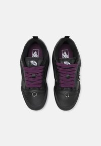 Svart skinnsneakers med lilla snörningar, vadderad krage och runda metallackenter. Tvåfärgad design med Vans-logotyp på innersulorna.