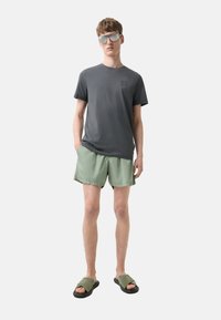 Grå kortærmet T-shirt, lysegrønne shorts og grønne slidesandaler. Modellen bærer reflekterende solbriller. Simpelt design, afslappet stil.