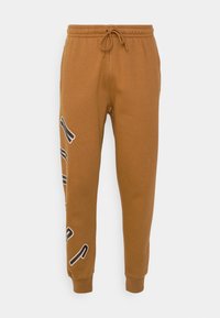 Bruna joggerbyxor med elastisk midja och dragsko, med svart och vit grafisk text på vänster ben och avslutade anklar.