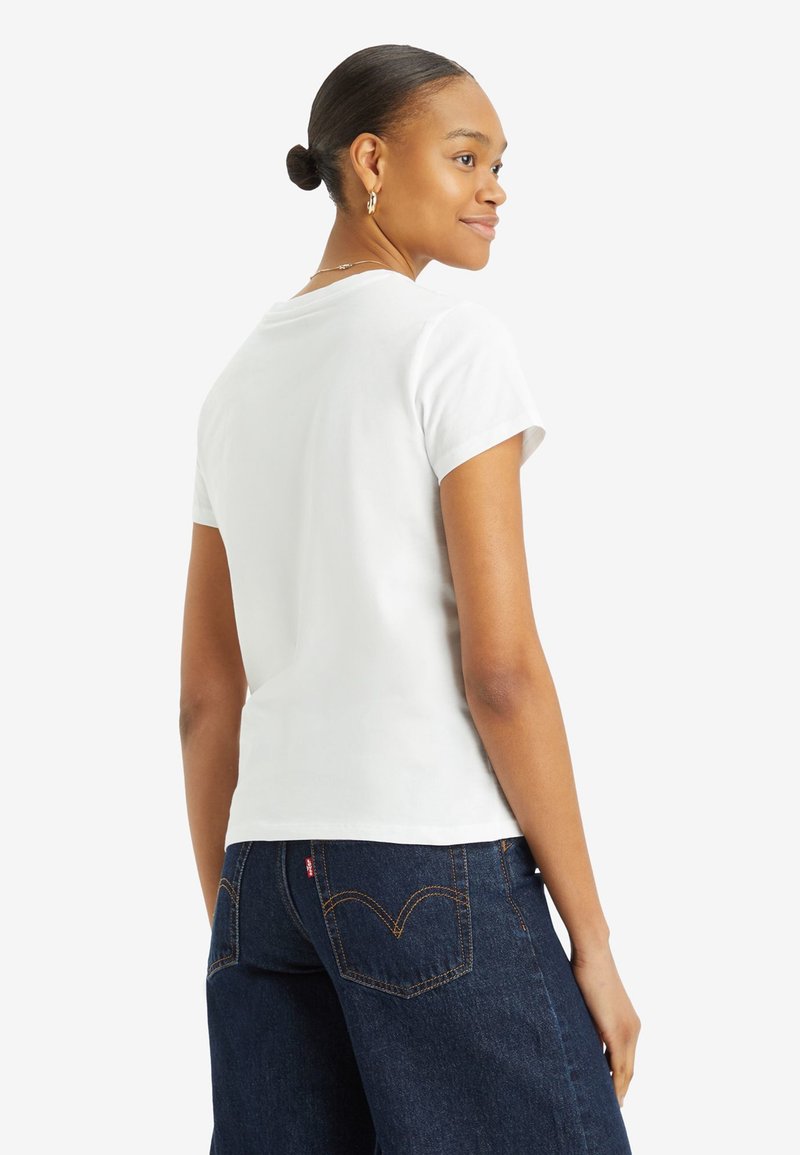 T-shirt en coton blanc à manches courtes et col ras du cou, affiché de dos. Associé à un jean en denim bleu foncé avec des accents brodés.
