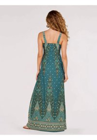 Robe longue sans manches de couleur sarcelle avec un motif cachemire. Elle présente des bretelles décoratives, un corsage ajusté et une jupe fluide ornée de bordures complexes.