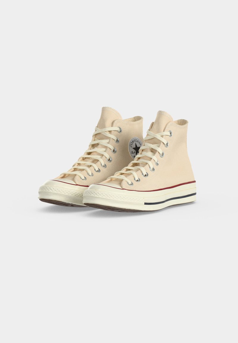 Ein Paar beigefarbene Converse High-Top-Sneaker mit weißen Schnürsenkeln, Gummisohlen und klassischem Logo an der Seite, nebeneinander platziert.