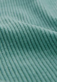 Tessuto di velluto a coste turchese con sottili righe verticali, texture morbida e una leggera lucentezza, che mostra un primo piano dei dettagli del materiale.