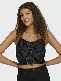 Černý crop top s velkou saténovou mašlí vpředu, zdobený flitry, a přiléhavým střihem. V kombinaci s černými kalhotami s vysokým pasem.