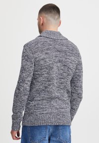 Strikket sweater i mørkegrå og sort med en tekstureret overflade, sjalskrave, lange ærmer samt ribbet kant og manchetter. Vist set fra ryggen.
