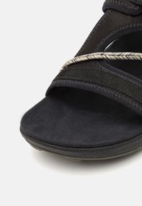Svart sandaled med en myk semsket fotseng, med tekstilremmer og en vridd metallikk accent. Åpen tå-design med polstret såle.
