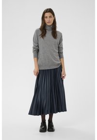 Maglione grigio a collo alto abbinato a una gonna midi plissettata blu navy. Le scarpe nere e le calze completano il look, con una texture liscia.