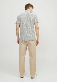 Camicia a maniche corte con bottoni, base bianca e motivo astratto nero, abbinata a pantaloni beige chiaro e sneakers casual.