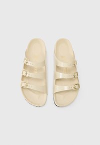 Beige sklidesandaler laget av glinsende materiale har tre justerbare stropper med gullspenner. Sålene er teksturerte for bedre grep.