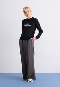 Črna jopica s potiskom "Nike Sportswear", kombinirana s sivo širokima hlačami. Obleka ima sproščen kroj in gladek material.