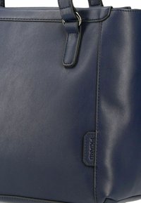 Blaues Ledertasche mit glatter Oberfläche, silbernem Beschlag, kurzen Trägern und einem Logo-Anhänger. Hat eine strukturierte Form und ein minimalistisches Design.