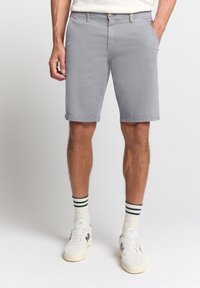 Grijze katoenen shorts met een relaxte pasvorm, contrasterende taillebanddetails en zijzakken, gecombineerd met witte sneakers en gestreepte sokken.