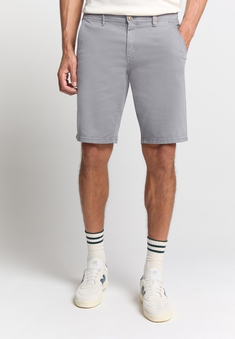 Grijze katoenen shorts met een relaxte pasvorm, contrasterende taillebanddetails en zijzakken, gecombineerd met witte sneakers en gestreepte sokken.