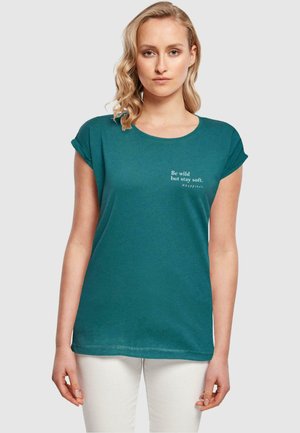 Türkises T-Shirt mit kurzen umgeschlagenen Ärmeln, rundem Halsausschnitt und weißem Text: "Sei wild, bleib aber sanft. #glück." Einfaches Design, weicher Stoff.